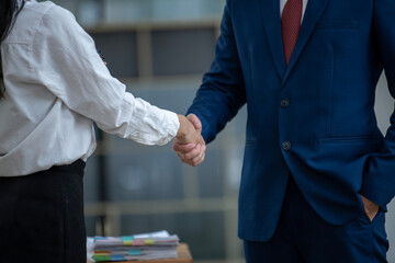 Close-up of a professional handshake between a male and female colleague over a desk with a laptop...