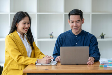 Professional Asian male and female colleagues discuss work on a laptop in a bright modern office,...