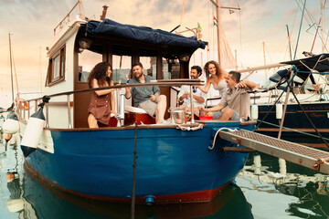 Friends share drinks and laughs on a classic boat at sunset, creating a picturesque and relaxed...