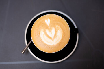Cup of cappuccino with latte art. Coffee in black cup on dark table in cafe. Food banner