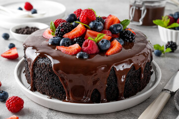Delicious chocolate cake with chocolate glaze and fresh berries on a white plate on a gray concrete background.