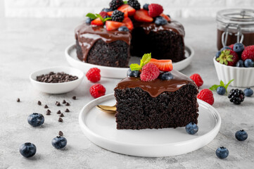 Delicious chocolate cake with chocolate glaze and fresh berries on a white plate on a gray concrete background.