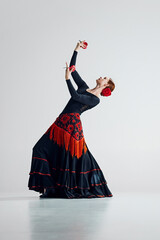 Theatrical and expressive, female flamenco dancer dancing with passion against grey studio...