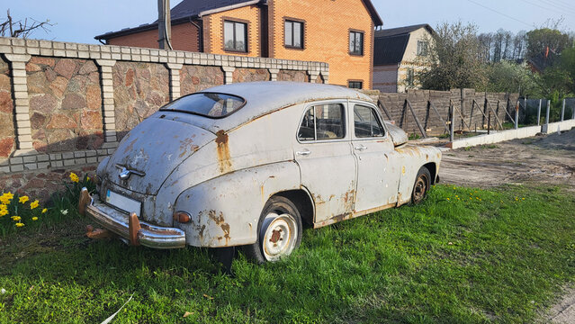 Nice old rusty soviet car Volga on green grass near the building at sunny evening, april 2024 Ukraine