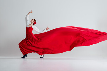 Sweeping elegance. Female dancer in striking red costume performing flamenco dance against grey...