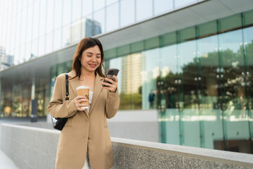 Business entrepreneur asian woman drink coffee use smartphone outside city office building