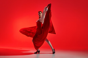 Female artistic flamenco dancer showing passion against striking red background. Elegant pose and...