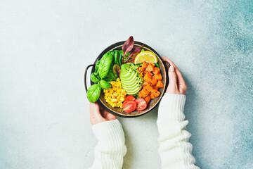 Woman's hands hold a bowl of Buddha: from pumpkin, avocado, corn and tomatoes, Healthy vegetarian dinner.