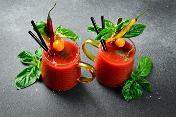 Fresh tomato juice with spices and basil in a cup. On a dark stone table.