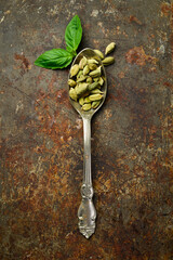 Fragrant cardamom seeds in a metal spoon. Spices and condiments. Top view. On a dark background.