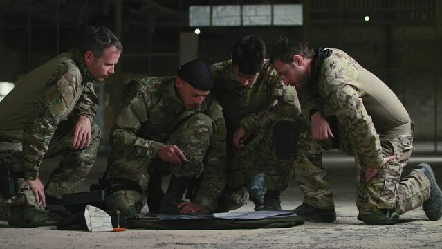 Soldiers kneeling around map and using laser pointer indoors