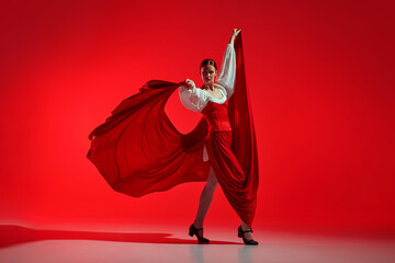 Passion in every step. Elegant woman, professional dancer performing flamenco against striking red...