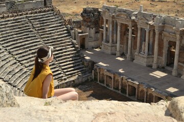 A girl sitting on a mountain admires the ruins of an ancient city. Ancient architecture, archeology. Travel, tourism, excursions. Turkey. Pamukkale, Hierapolis.