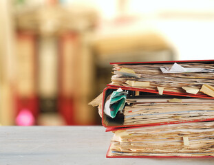 stack of dusty messy file folders with narrow depth of field, blurred office in the back,red tape,...
