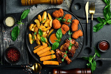 Beer snack plate: chicken nuggets, chicken wings, cheese and fries. On a dark background, close-up.