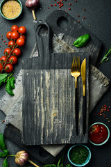 Creative kitchen banner. Cutting board, cutlery, spices and kitchen utensils on black stone...