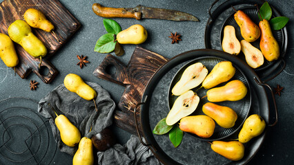 Pears on plates. There are slices of pears and a knife on the cutting board. Top view. On a black stone background.
