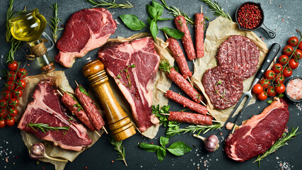 A set of juicy raw steaks, kebabs, cutlets and meat with spices and herbs. On a black stone...