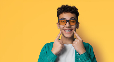 Dental dent care ad concept image - сurly haired funny young man wear metal braces, sunglasses...