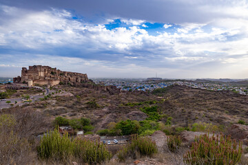 Fototapeta na wymiar ancient historical fort with blue colored city houses and dramatic cloudy sky at evening