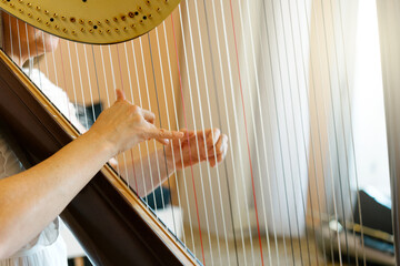 Hands of a professional harpist playing a traditional harp.