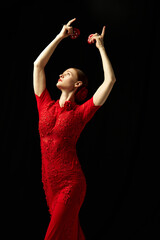 Elegant woman in beautiful red dress performing with castanets against black background. Following...
