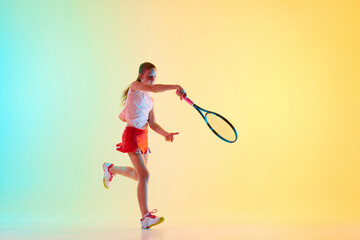 Portrait of young sportive girl, teenage tennis player in uniform training in motion in neon light...