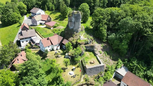 Flight towards craggy hill spur Bergschmidtsknock with summit cross at ruin of B&auml;rnfels Castle near Obertrubach in Franconian Switzerland, Germany