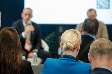 An engaging business presentation at a conference, featuring a speaker addressing an attentive audience. Professionals listening intently in a seminar room.