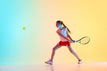 Sportive teen girl, tennis athlete training skills of hitting ball from opponent in neon light...