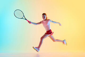 Portrait of young girl, teen tennis player in uniform training hitting ball in neon light against...