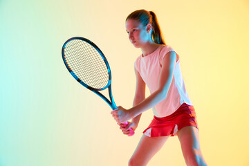 Young athletic teenage girl, tennis player stand ready to start competition in neon light against...