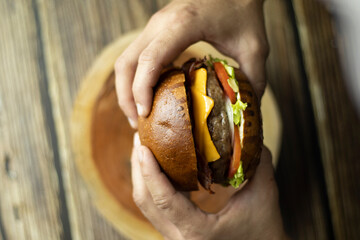 Duas mãos segurando um hamburguer em cima de uma mesa de madeira Two hands holding a burger on a...