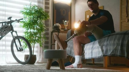 Young amputee man putting on prosthesis leg sitting on the bed early in the morning