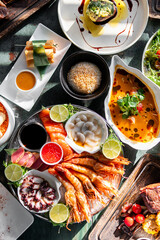 An elegant spread of gourmet dishes, including grilled prawns, scallops, spring rolls, and a rice-based delicacy, beautifully presented on a dark green table