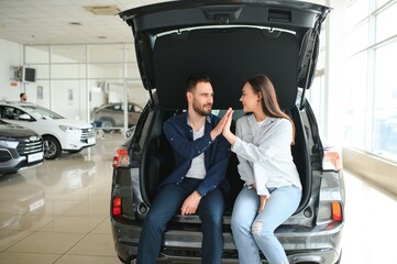 Happy young couple chooses and buying a new car for the family. Visitting the dealership