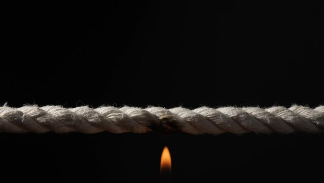 Burning rope at breaking point on dark background, closeup.