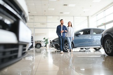 It is the one car I want. Beautiful young couple standing at the dealership choosing the car to buy
