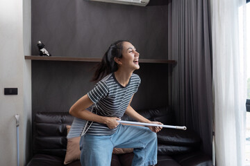 young asian woman having fun during cleaning, fooling with mop and broom