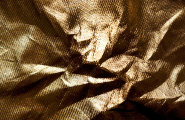 Background of goldy shiny foil fabric, detail closeup of textured wrapping  golden textile brocade