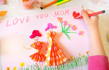 Child making homemade greeting card. little girl making card for mom with flowers from paper as...