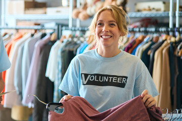 Female Charity Worker Checking Clothing Donations At Thrift Store