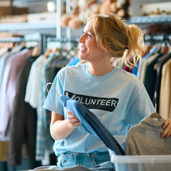 Female Charity Worker Sorting Clothing Donations At Thrift Store