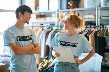 Male And Female Charity Volunteers Working Sorting Through Donations Of Clothing At Thrift Store