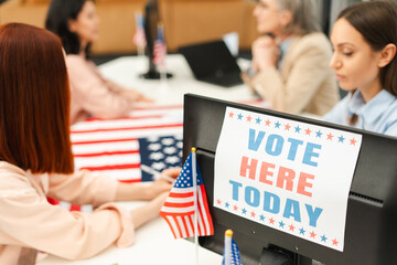 Voter sitting at registration table, registering at polling station decorated with American flag