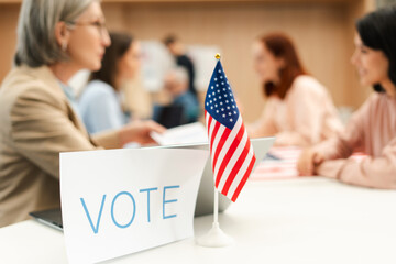 Group of US citizens voting at polling station selective focus on American flag