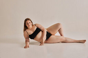 Fototapeta premium Strength of beauty. Young woman comfortable in her own skin, promoting positive body image against grey studio background. Concept of natural beauty, body positivity, care, acceptance