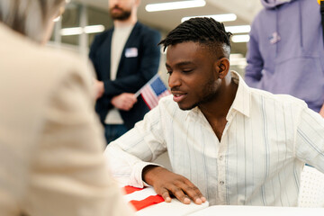 Attractive African American man, citizen, sitting at registration table decorated with American flag