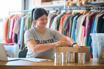 Female Charity Worker At Desk With Laptop Checking Food Donations At Foodbank