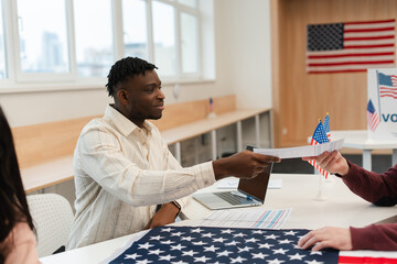Smiling happy African American young male worker working at polling station, holding ballot
